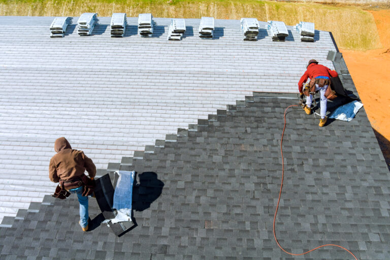 Worker hands installing bitumen roof shingles with air hammer and nail